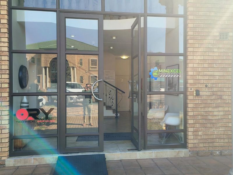 Main entrance to the office building featuring a glass and aluminium door, brick exterior facade, and a view into the interior lobby area.