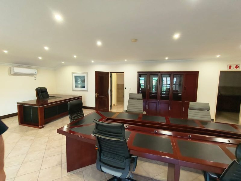A professional office space featuring tiled flooring, recessed downlighting, a wall-mounted air conditioning unit, and integrated wooden cabinetry.