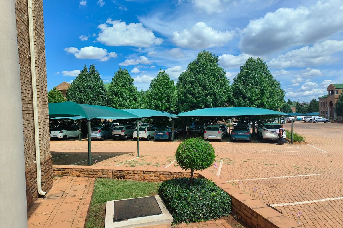 A paved outdoor parking area featuring multiple shade cloth carports and landscaped retaining walls.