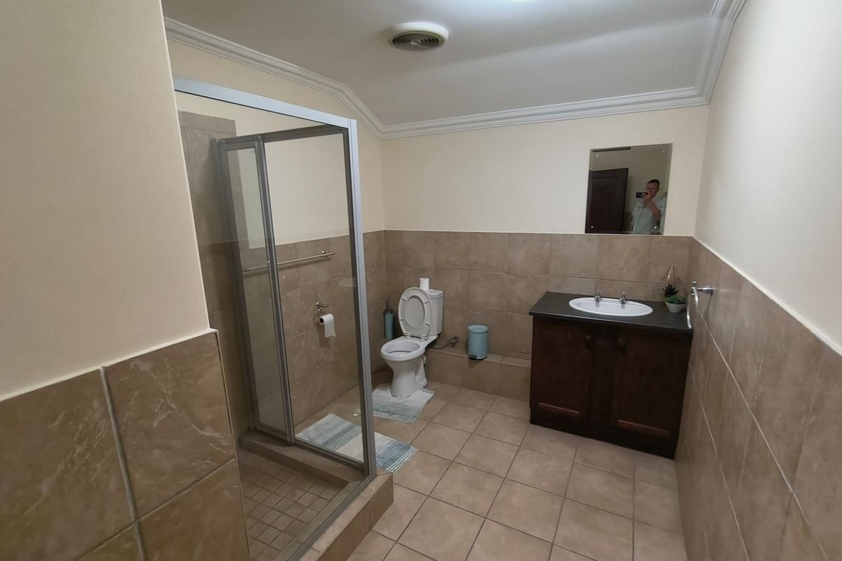 A functional bathroom featuring a shower enclosure, a vanity cabinet with a washbasin, and neutral wall and floor tiling.