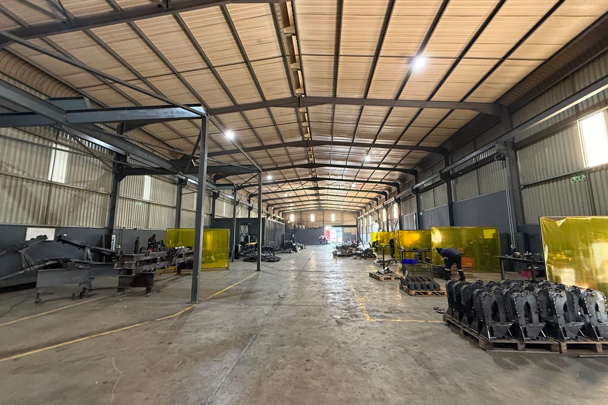 Spacious industrial warehouse featuring a high-clearance steel portal frame, concrete flooring, and functional high-bay lighting, suitable for manufacturing or storage operations.