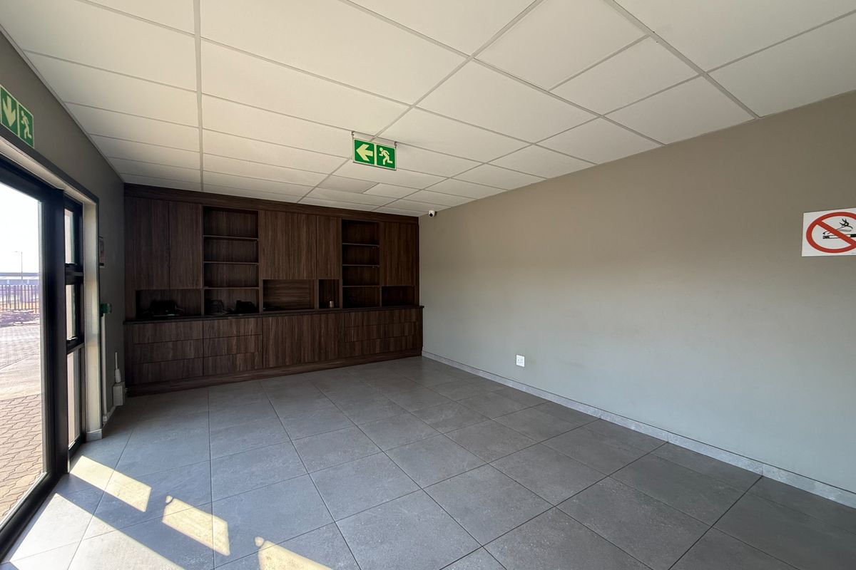A clean, modern office space featuring neutral tiled flooring, a suspended ceiling, and extensive built-in dark wood cabinetry for storage.