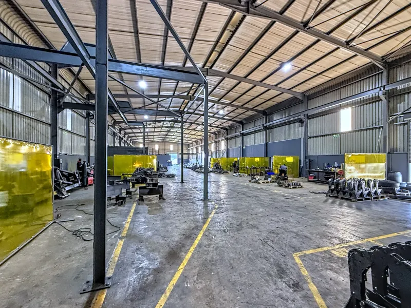 Spacious industrial warehouse facility featuring a steel portal frame structure, high ceilings, concrete flooring, and integrated welding bays with protective screens.
