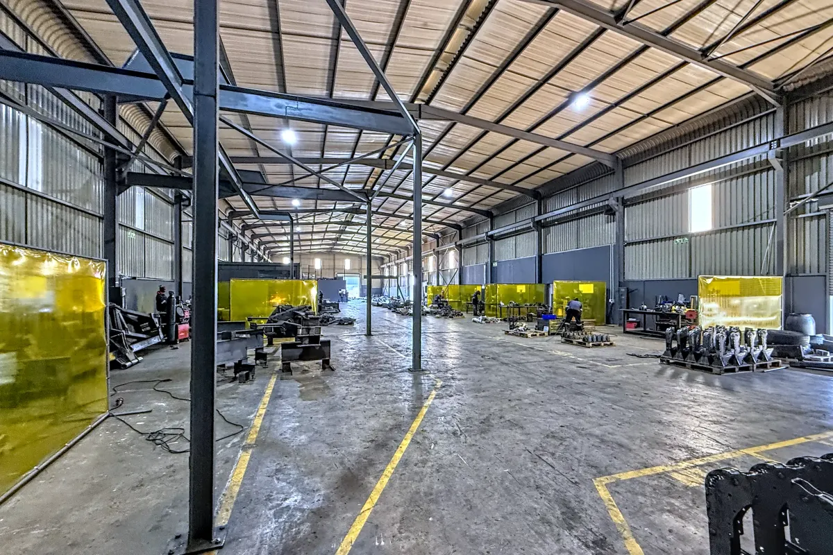 Spacious industrial warehouse facility featuring a steel portal frame structure, high ceilings, concrete flooring, and integrated welding bays with protective screens.