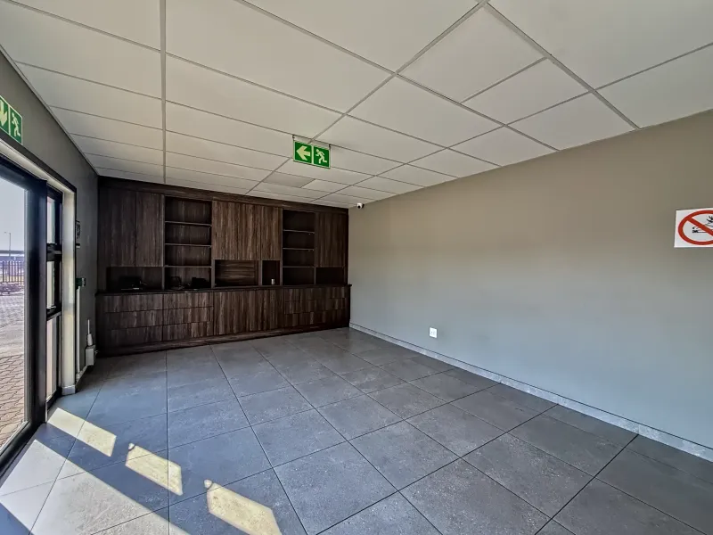 A clean, empty office space featuring modern tiled flooring, a suspended ceiling, and extensive built-in dark wood cabinetry.
