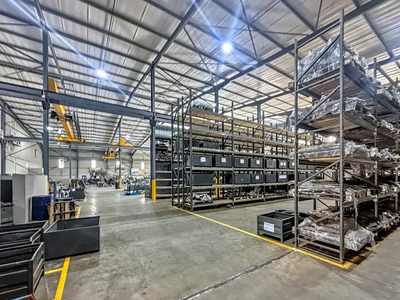 Spacious industrial warehouse featuring a high-clearance steel portal frame, overhead crane system, concrete flooring, and extensive built-in industrial racking for storage.