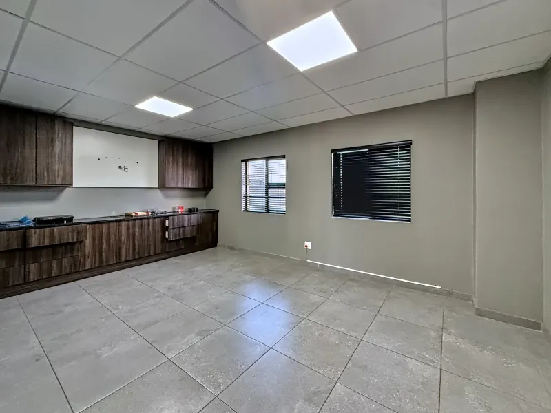 A clean, modern industrial kitchen space featuring dark wood-grain cabinetry, grey tiled flooring, and recessed ceiling lighting, offering a versatile and functional work area.