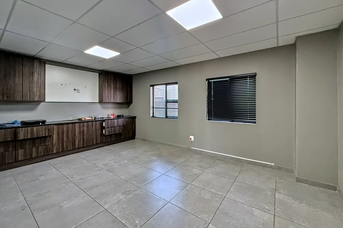 A clean, modern industrial kitchen space featuring dark wood-grain cabinetry, grey tiled flooring, and recessed ceiling lighting, offering a versatile and functional work area.
