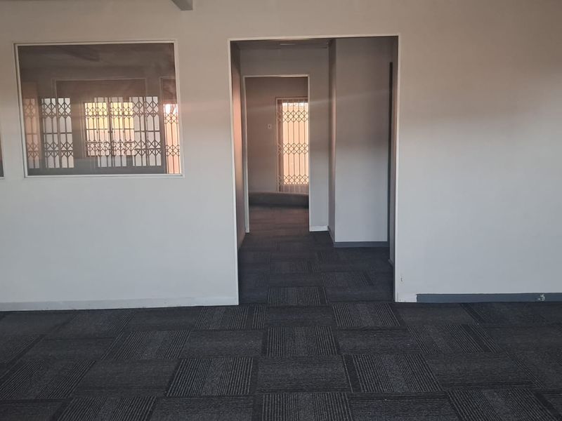 An empty office space featuring dark carpet tiles, internal glass partitions, and security gates, providing a clean and functional layout for professional use.