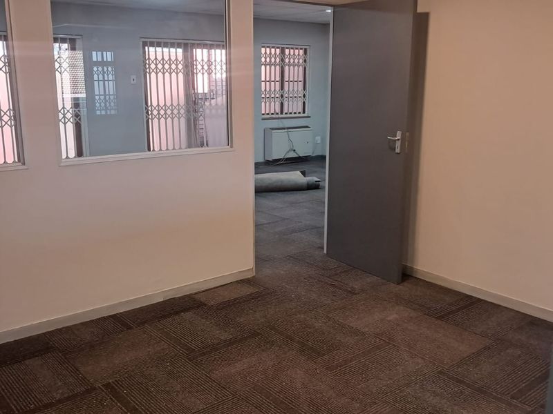 An empty office space featuring carpet tiles, internal glass partitioning, and security gates on the windows, providing a functional and secure workspace environment.