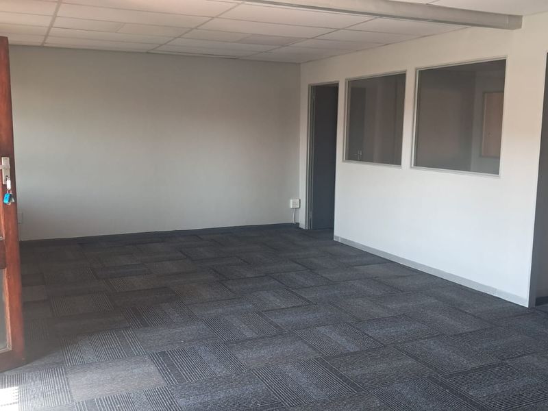 An empty office space featuring carpet tiles, a suspended ceiling, and glass partition windows, providing a clean and functional professional environment.