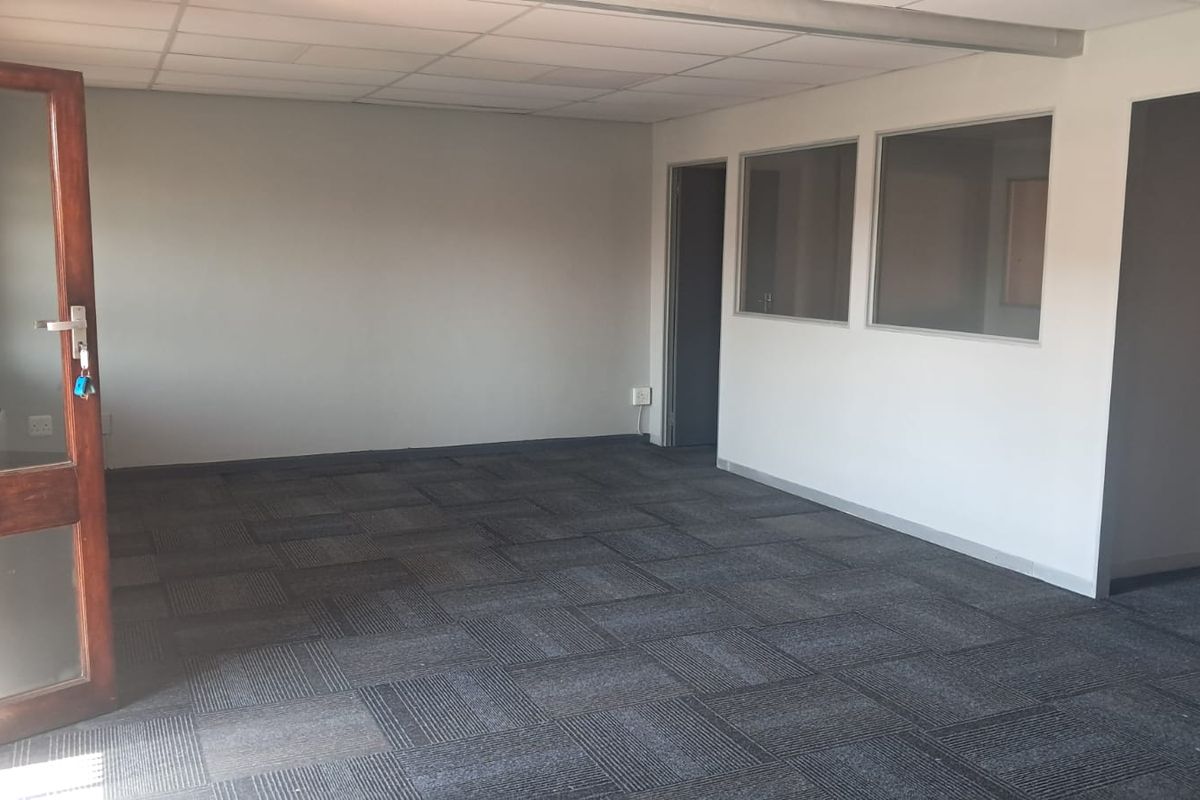 An empty office space featuring carpet tiles, a suspended ceiling, and glass partition windows, providing a clean and functional professional environment.