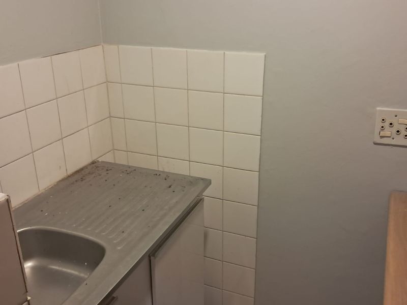 A small, functional kitchen area featuring a stainless steel sink, tiled splashback, and built-in cabinetry, suitable for a compact office utility space.