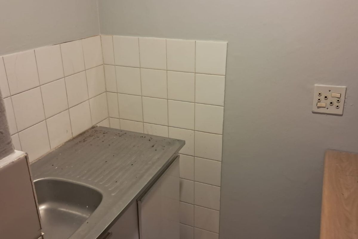 A small, functional kitchen area featuring a stainless steel sink, tiled splashback, and built-in cabinetry, suitable for a compact office utility space.