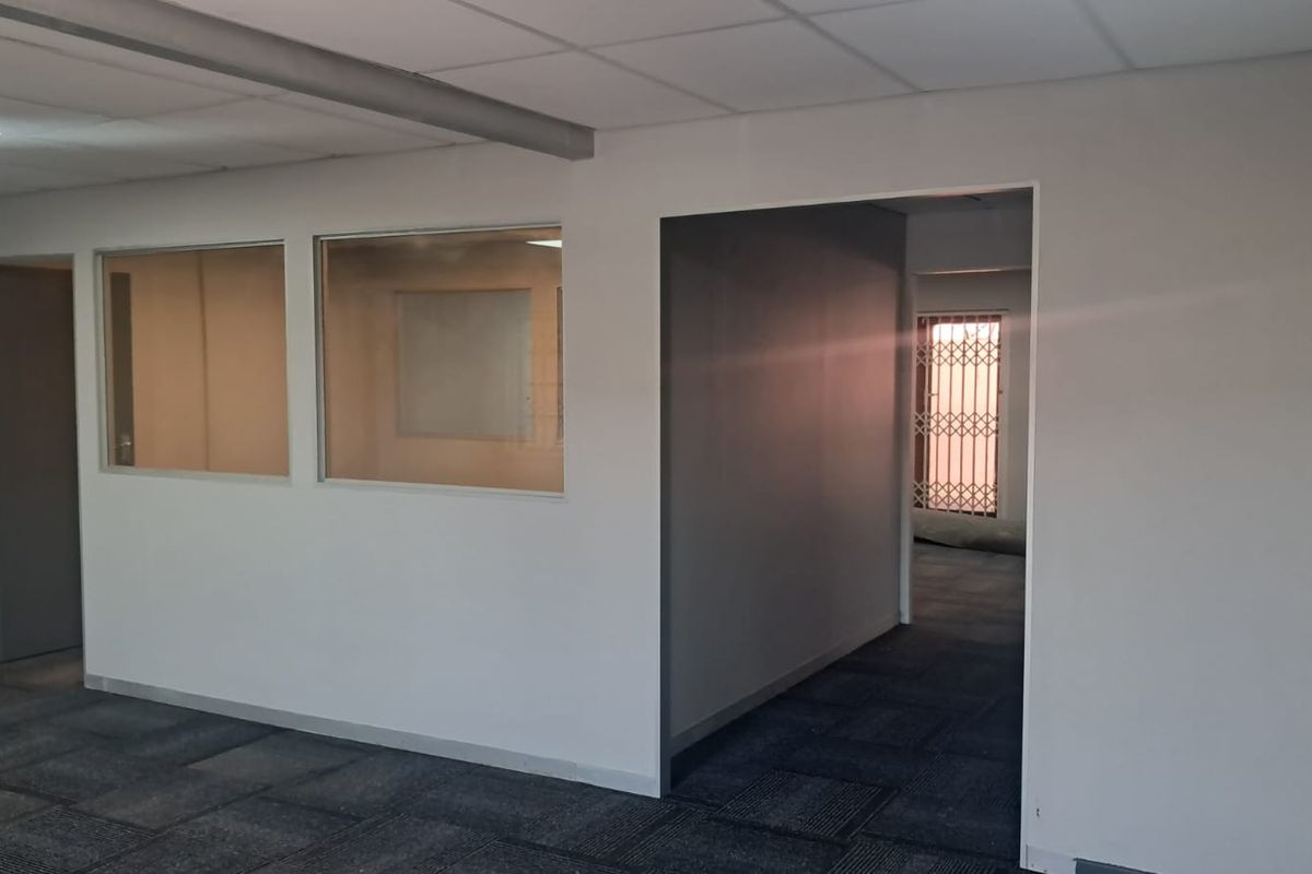 An empty office space featuring neutral walls, carpet tiles, suspended ceilings, and internal glass partitions providing a professional layout.