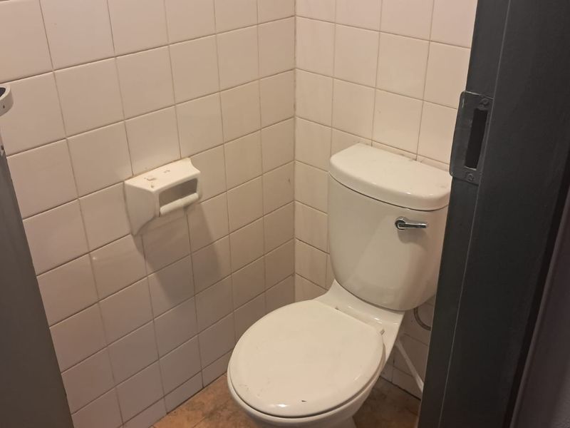 A small, functional office restroom featuring white ceramic wall tiles and a standard toilet fixture.
