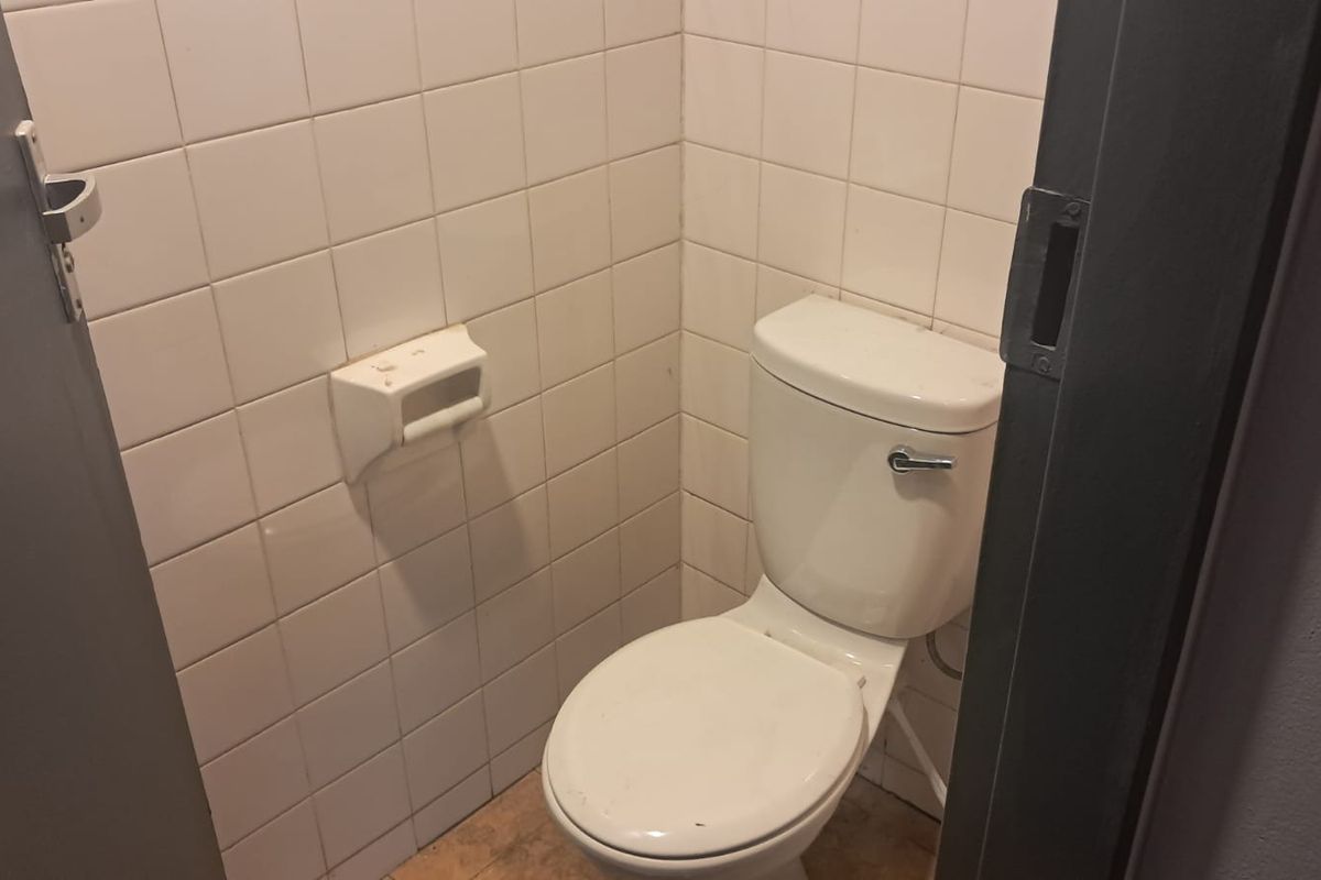 A small, functional office restroom featuring white ceramic wall tiles and a standard toilet fixture.