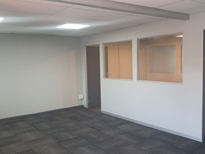 A clean, vacant office space featuring neutral walls, carpet tile flooring, a suspended ceiling with recessed lighting, and an internal glass partition wall.