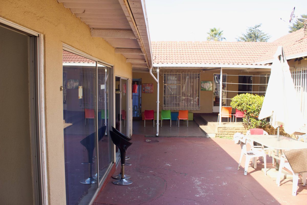 A covered outdoor patio area featuring tiled flooring, sliding glass door access, and security bars on windows, suitable for an outdoor business break area.