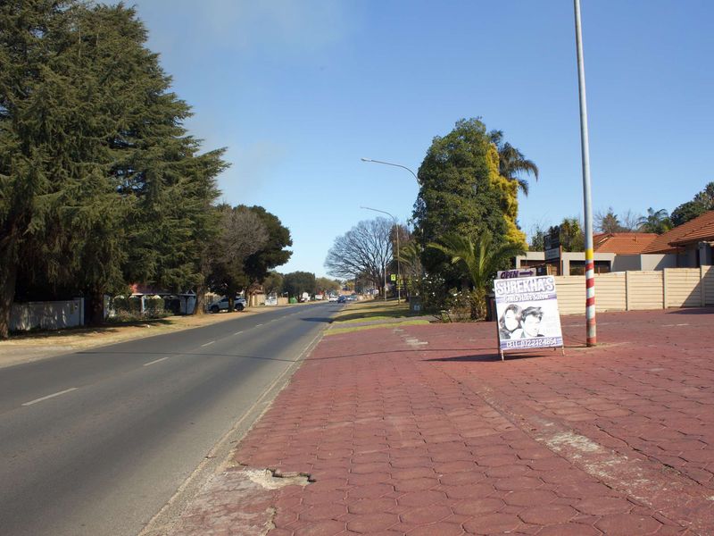 Street view showing the paved sidewalk, boundary wall, and surrounding neighbourhood approach.