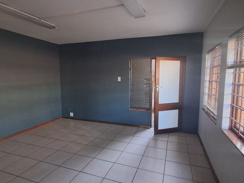 A vacant office space featuring tiled flooring, large windows with security bars, venetian blinds, and dark-toned walls.