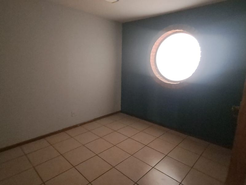 An empty office space featuring tiled flooring and a distinctive circular window, providing a blank canvas for a professional workspace.