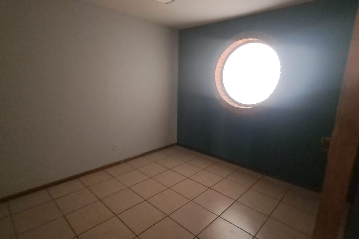An empty office space featuring tiled flooring and a distinctive circular window, providing a blank canvas for a professional workspace.