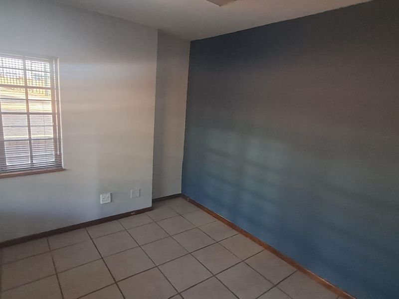 A vacant office space featuring tiled flooring, a window with security bars, and a dark accent wall.