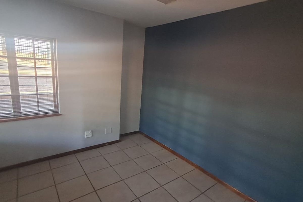 A vacant office space featuring tiled flooring, a window with security bars, and a dark accent wall.