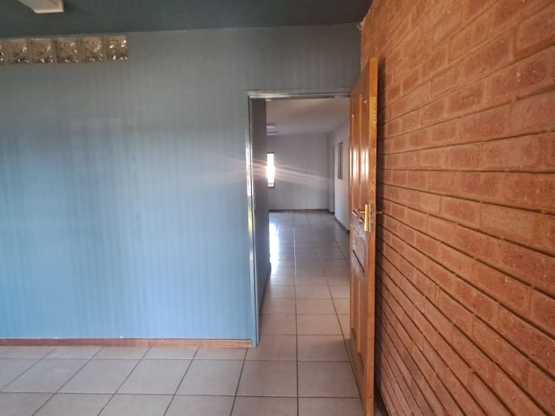An empty office space featuring a combination of painted walls, an exposed brick feature wall, glass block accents, and tiled flooring.