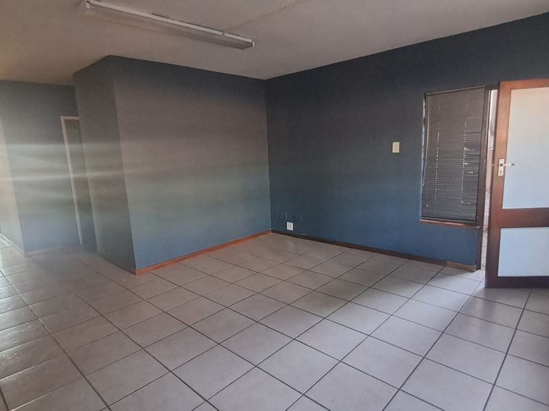 An empty office space featuring ceramic floor tiles, dark painted walls, and a timber door with integrated glass panels.