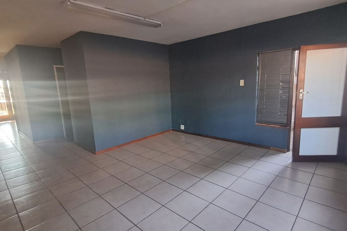 An empty office space featuring ceramic floor tiles, dark painted walls, and a timber door with integrated glass panels.