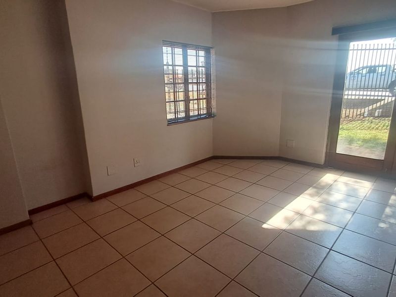 A vacant office space featuring neutral tiled flooring, natural light, and direct access to the exterior through a secure glass door.