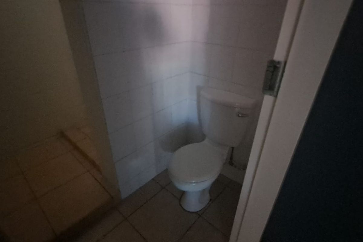 A small, functional bathroom featuring tiled walls and flooring with a standard toilet, currently in need of modernization and improved lighting.