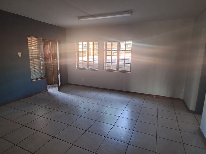 A bright, empty office space featuring tiled flooring, security gates, and large windows allowing for ample natural light.
