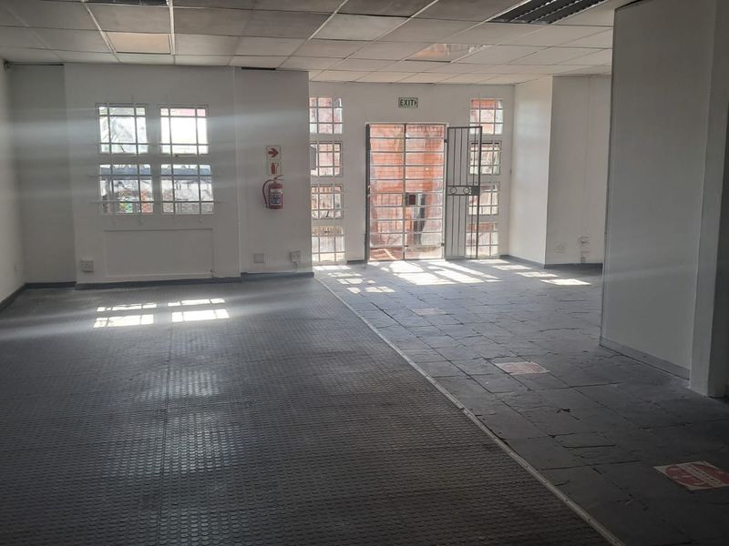An empty, open-plan office space featuring a suspended ceiling, security gate, and a mix of tiled and rubberized flooring.