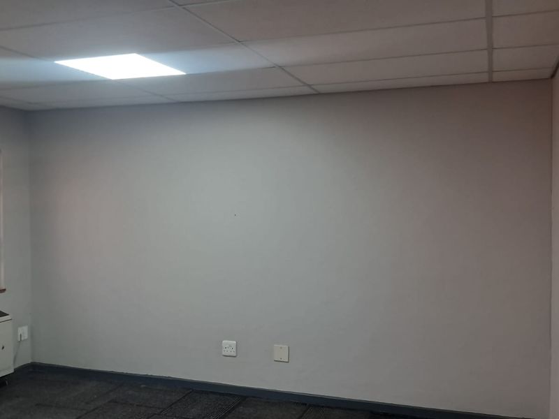 A vacant office space featuring a suspended ceiling with recessed lighting, carpeted flooring, and a window fitted with a security gate.