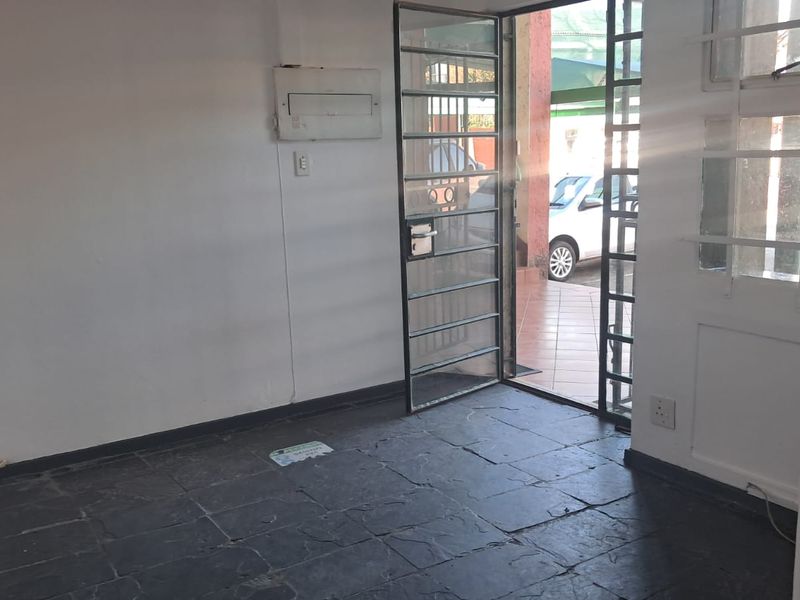 An empty office space featuring dark tiled flooring, a security gate entrance, and built-in electrical distribution board.