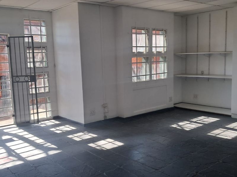 A vacant office space featuring tiled flooring, built-in shelving, integrated cabinetry, and secure window bars, offering a functional layout for professional use.