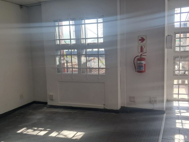 An empty office space featuring security bars on windows, a wall-mounted fire extinguisher, and tiled flooring, suitable for a professional workspace.