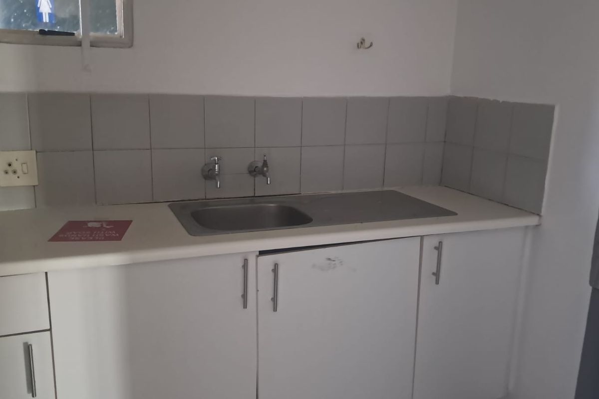 A small office kitchenette featuring a stainless steel sink, laminate countertop, and built-in white cabinetry with a tiled backsplash.