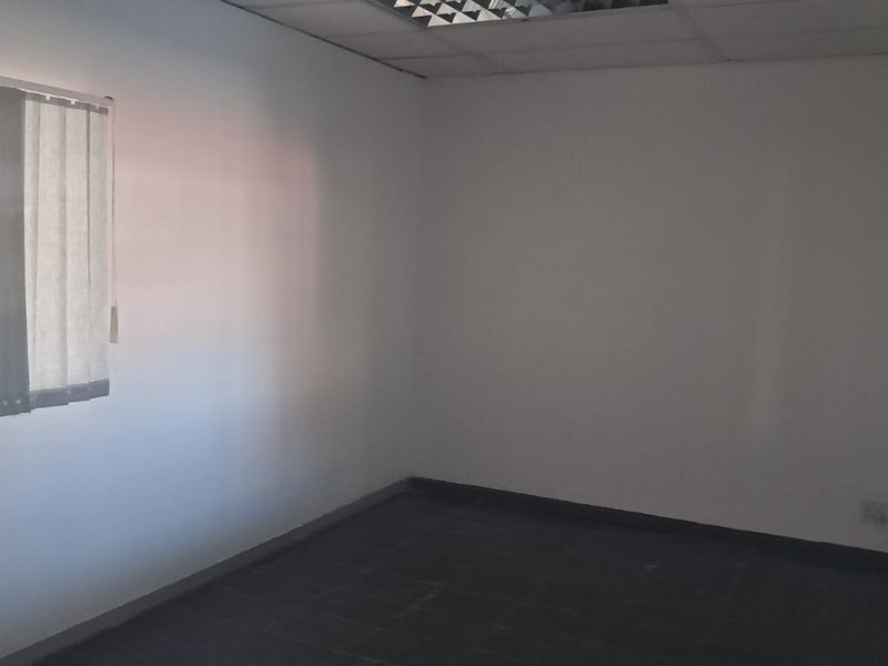 An empty office space featuring a suspended ceiling, tiled flooring, and vertical blinds on the window.