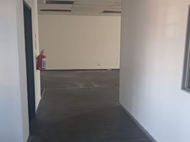 An empty office space featuring a suspended ceiling with missing tiles, neutral walls, and an internal glass partition.