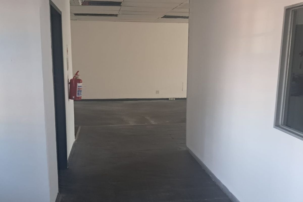 An empty office space featuring a suspended ceiling with missing tiles, neutral walls, and an internal glass partition.