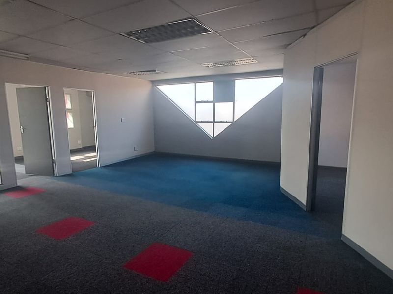 An empty office space featuring a unique triangular window, suspended ceiling, and carpeted flooring, offering a versatile layout for professional use.