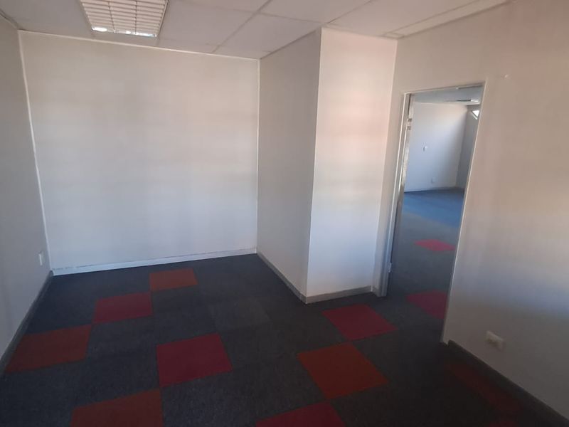 An empty office space featuring a suspended ceiling, recessed lighting, and patterned carpet tiles, providing a functional layout for professional use.