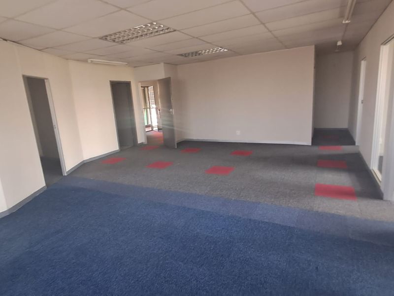An empty, open-plan office space featuring suspended ceilings, recessed lighting, and multi-colored carpet tiles, offering a versatile layout for professional use.