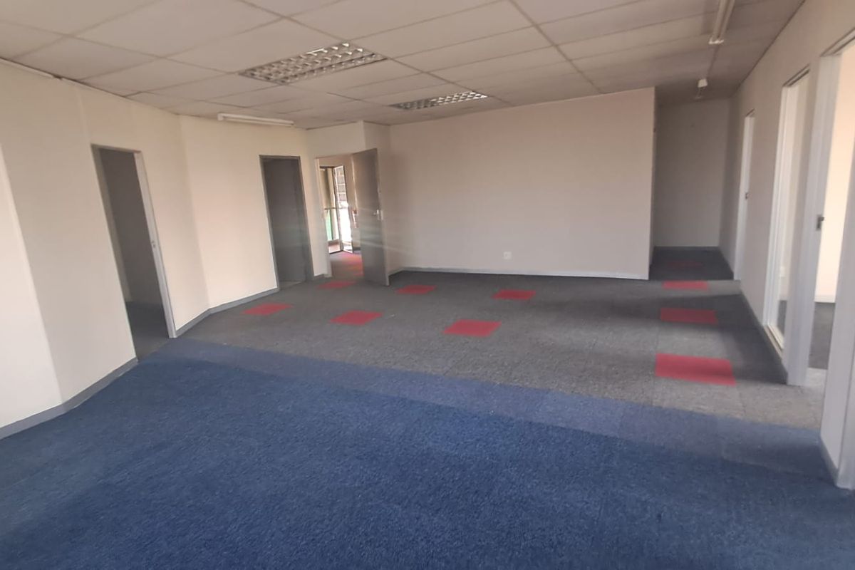 An empty, open-plan office space featuring suspended ceilings, recessed lighting, and multi-colored carpet tiles, offering a versatile layout for professional use.