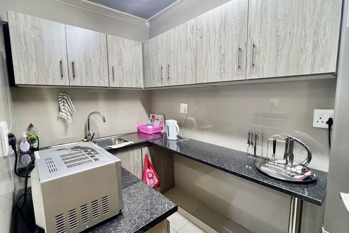 Compact kitchen area featuring light wood-grain cabinetry, dark granite countertops, a stainless steel sink, and tiled splashbacks.