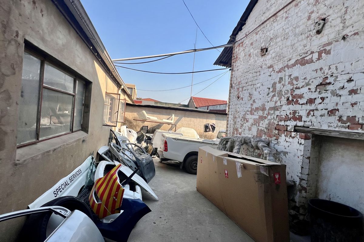 Rear exterior yard area featuring concrete paving and industrial brick walls showing significant signs of wear and weathering.